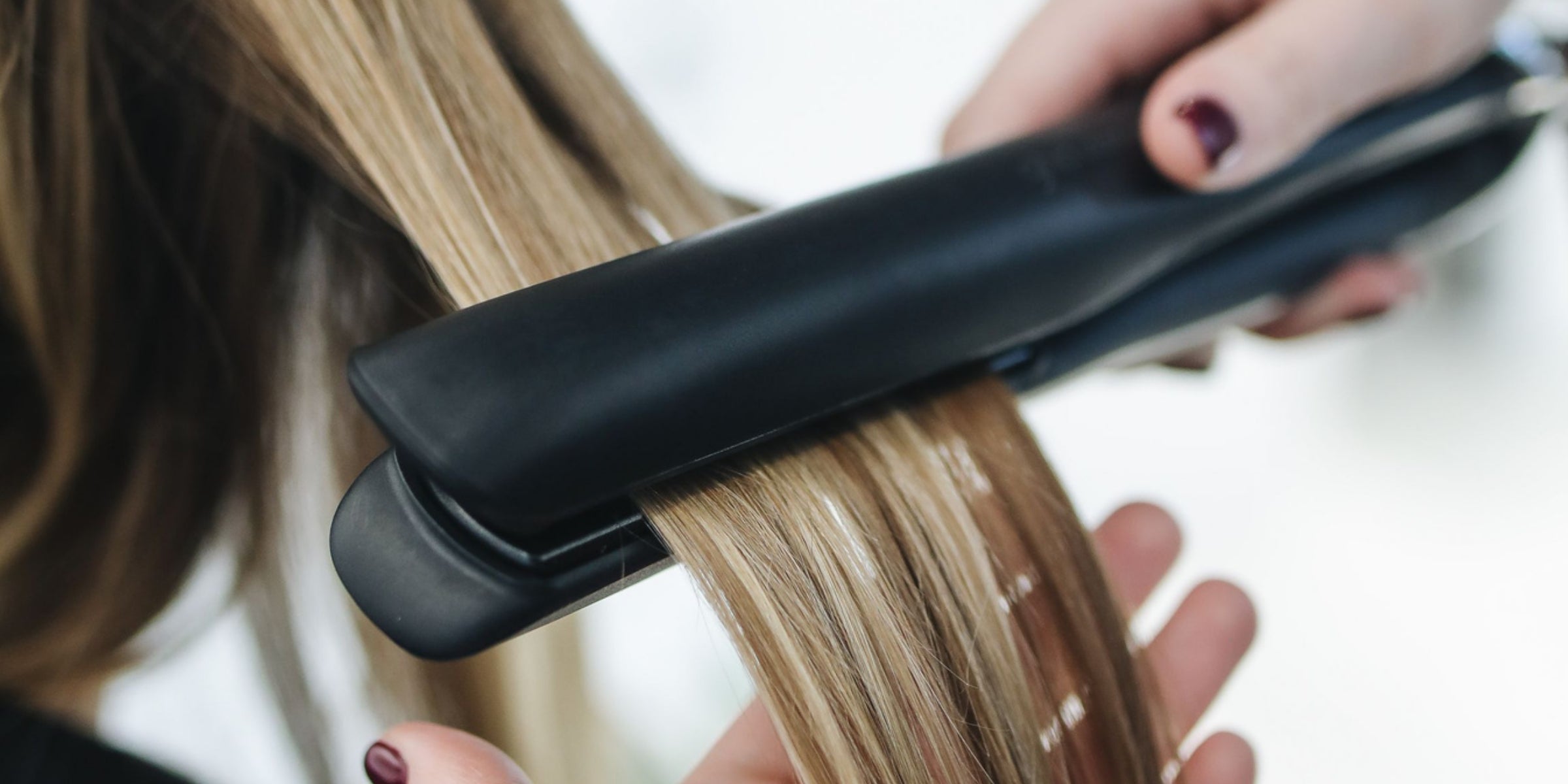 Hands styling long hair using a flat iron