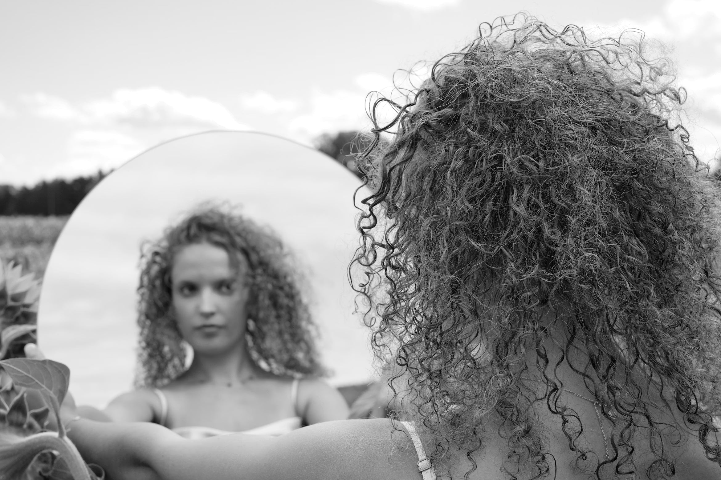 A woman with flat curly hair looking in a mirror.